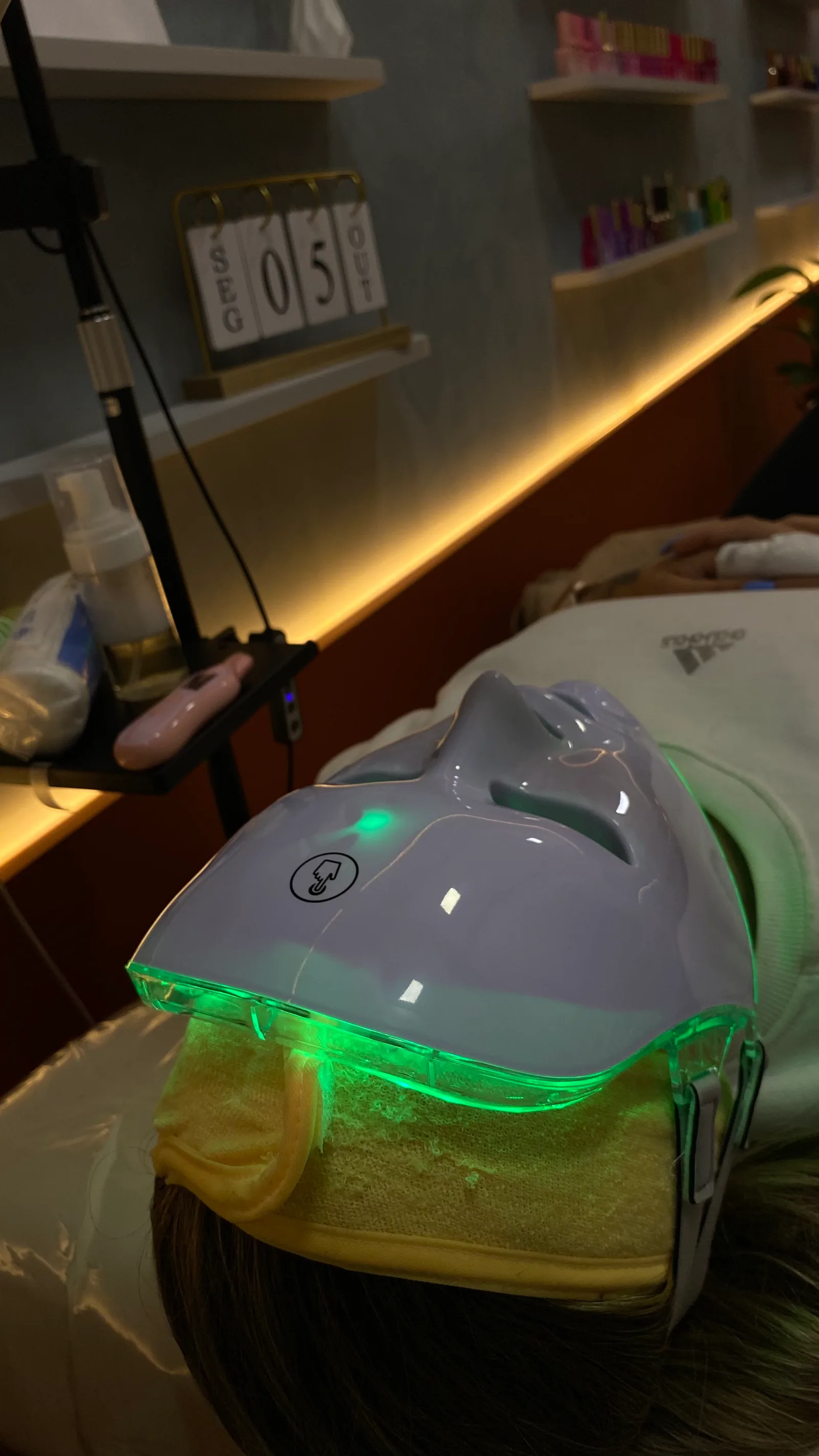 Cliente deitada com máscara de LED verde durante o cuidado com a pele, em ambiente com luz quente
